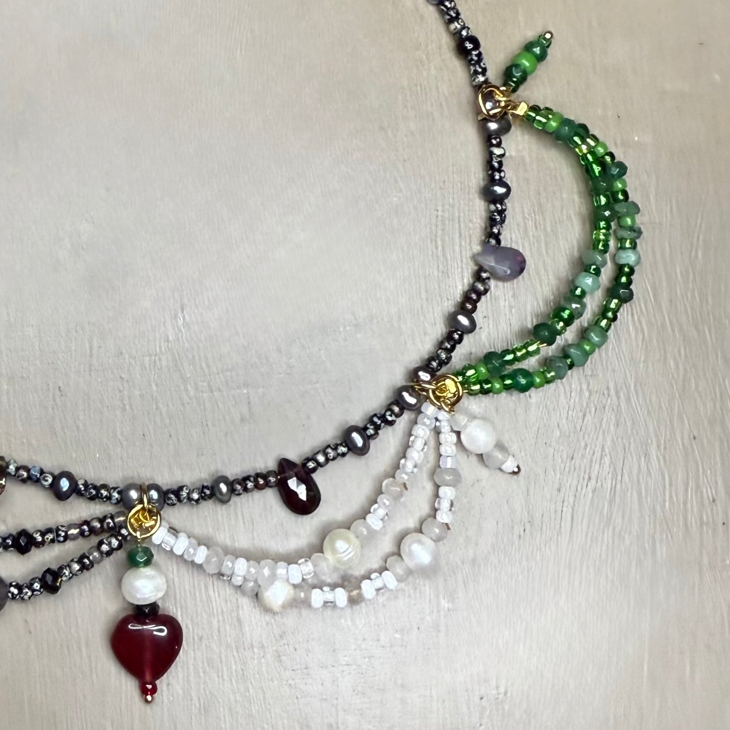 Multistrand beaded necklace with green, black, and white gemstones on a light wooden surface