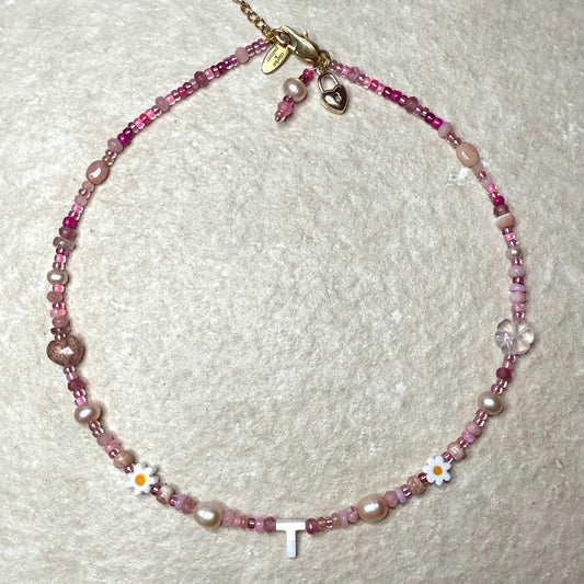 Detail of Necklace with pink gemstone beads and a letter 'T' on a textured white background
