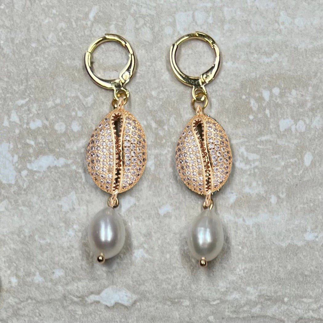 Gold Cowrie Shell earrings with pearl drops on a textured gray background