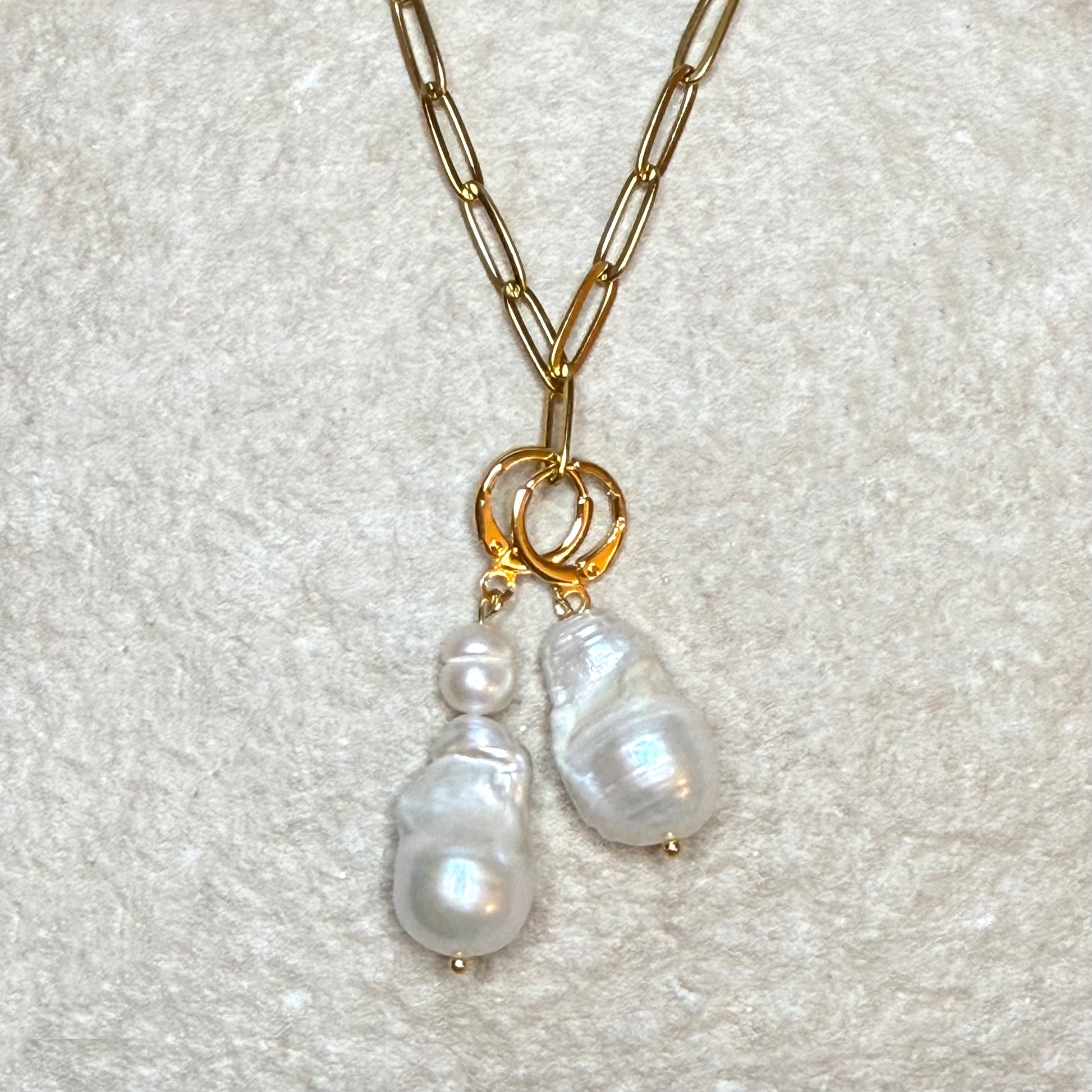 Gold chain necklace with pearl pendants on a textured white background