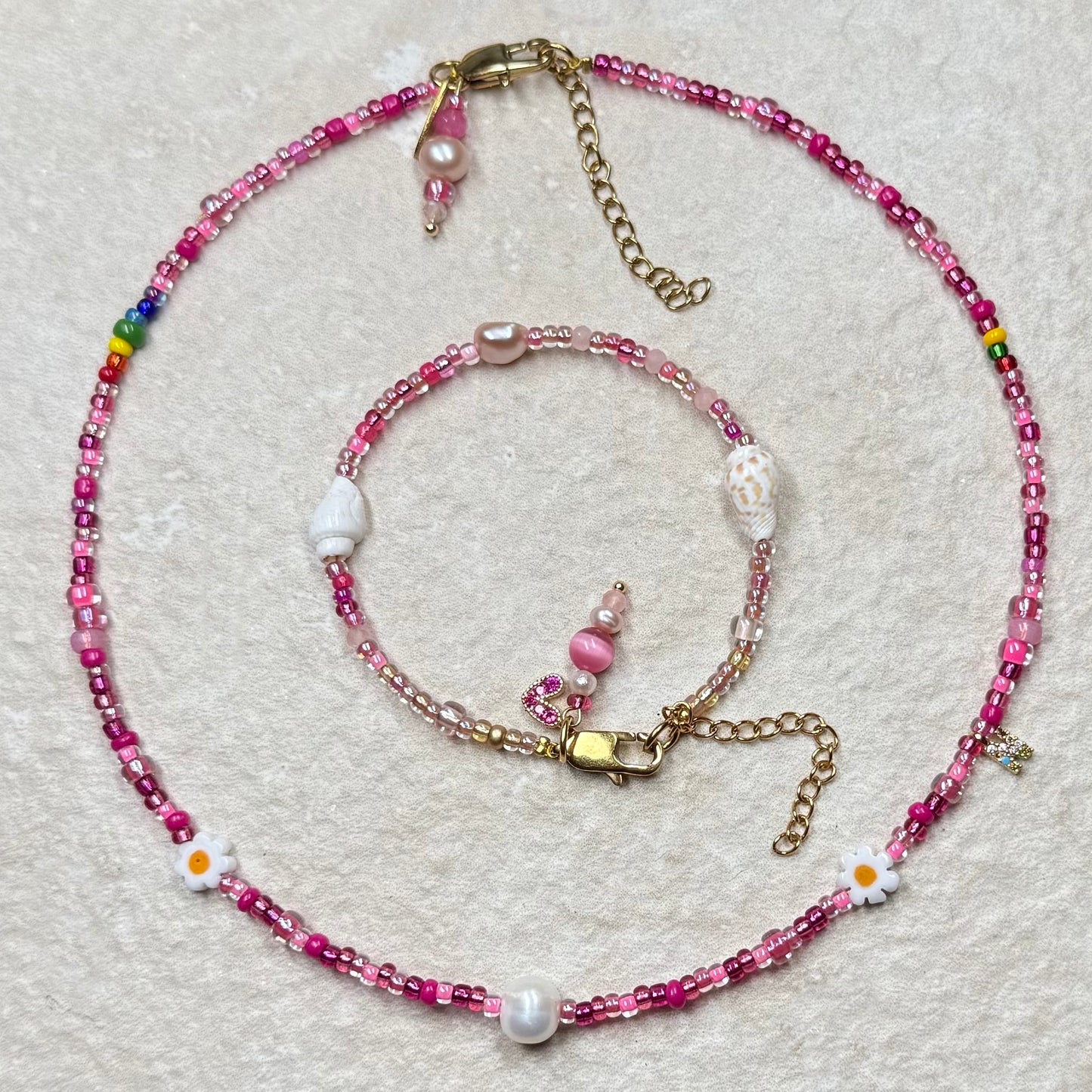 Beaded necklace and bracelet set with pink and gold accents on a light gray background