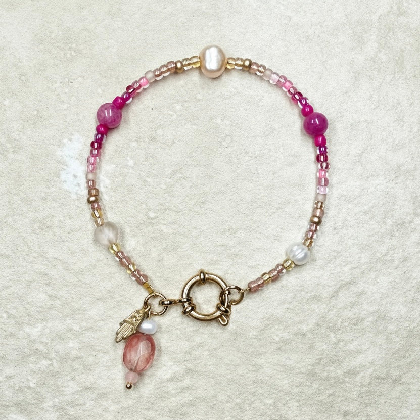 Beaded bracelet with pink and gold elements on a textured beige background