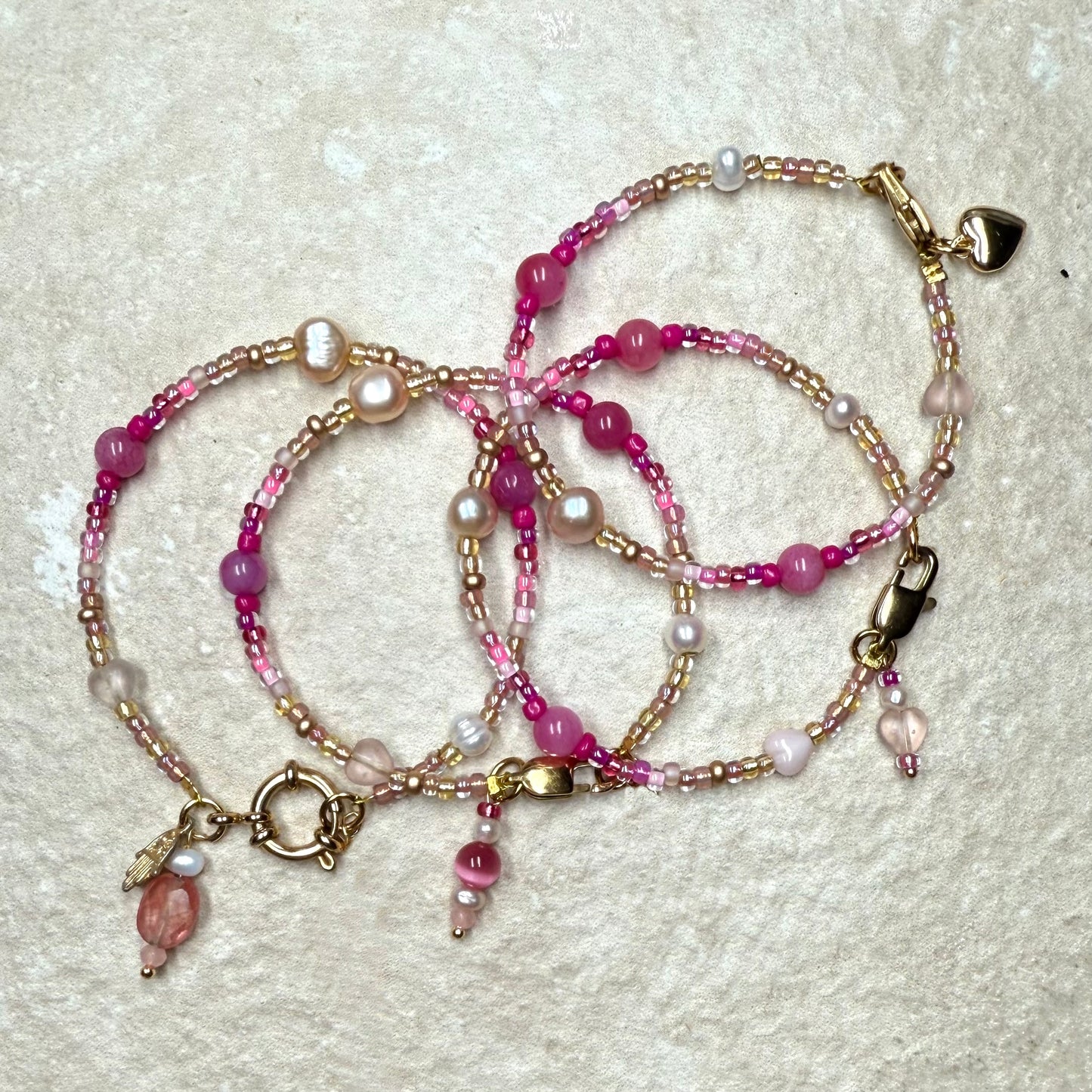 Set of beaded bracelets with pink and gold accents on a textured surface
