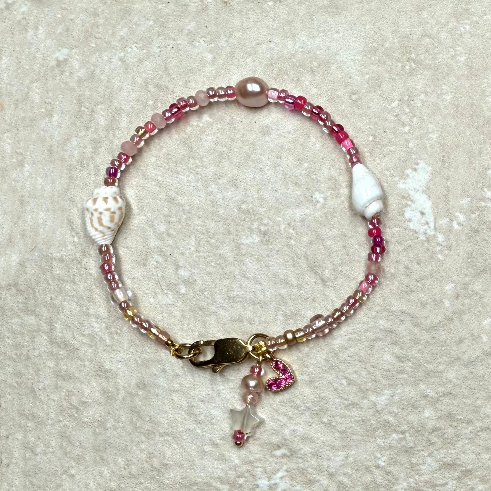 Beaded bracelet with shell and heart charms on a textured surface