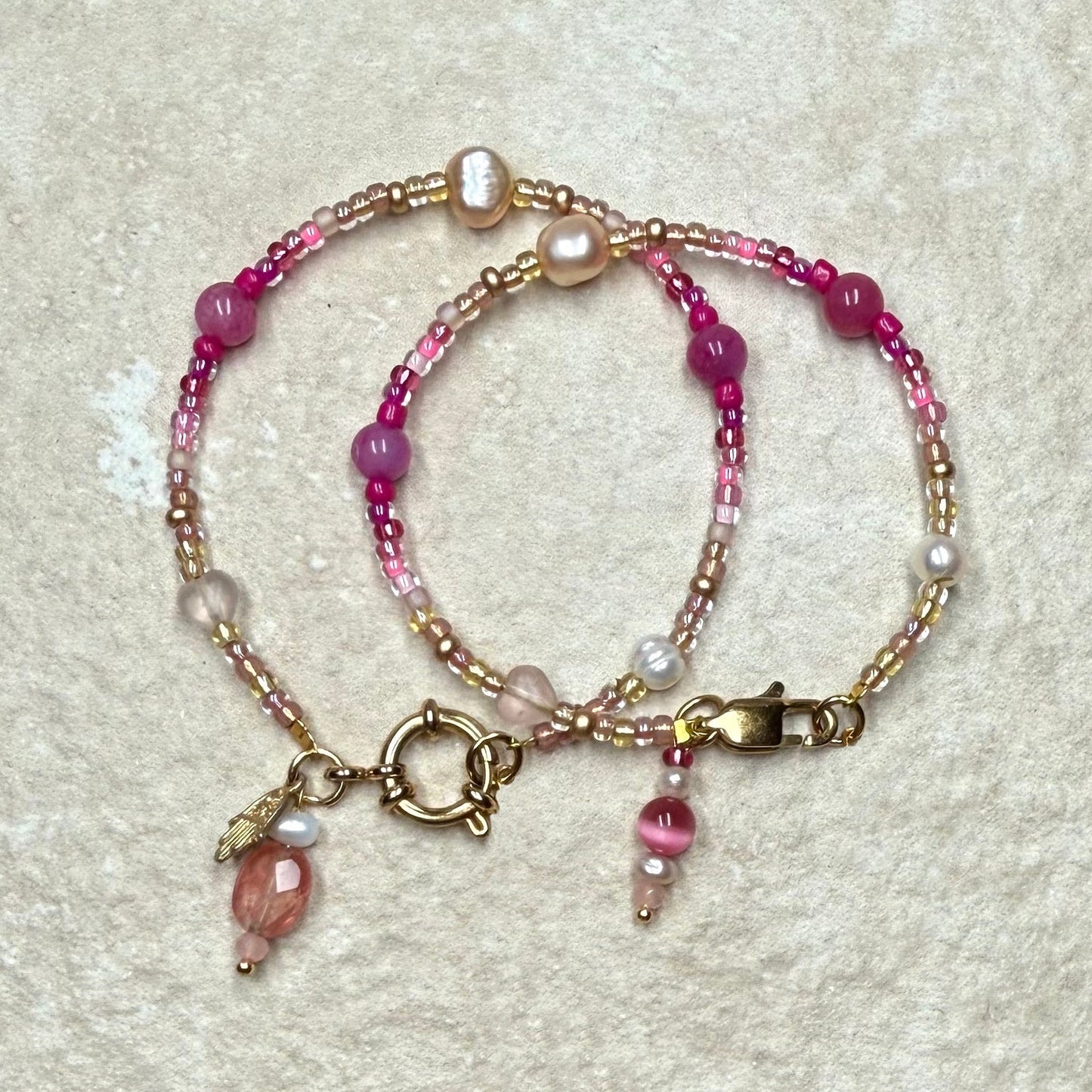 Beaded bracelet with pink and gold elements on a textured beige surface