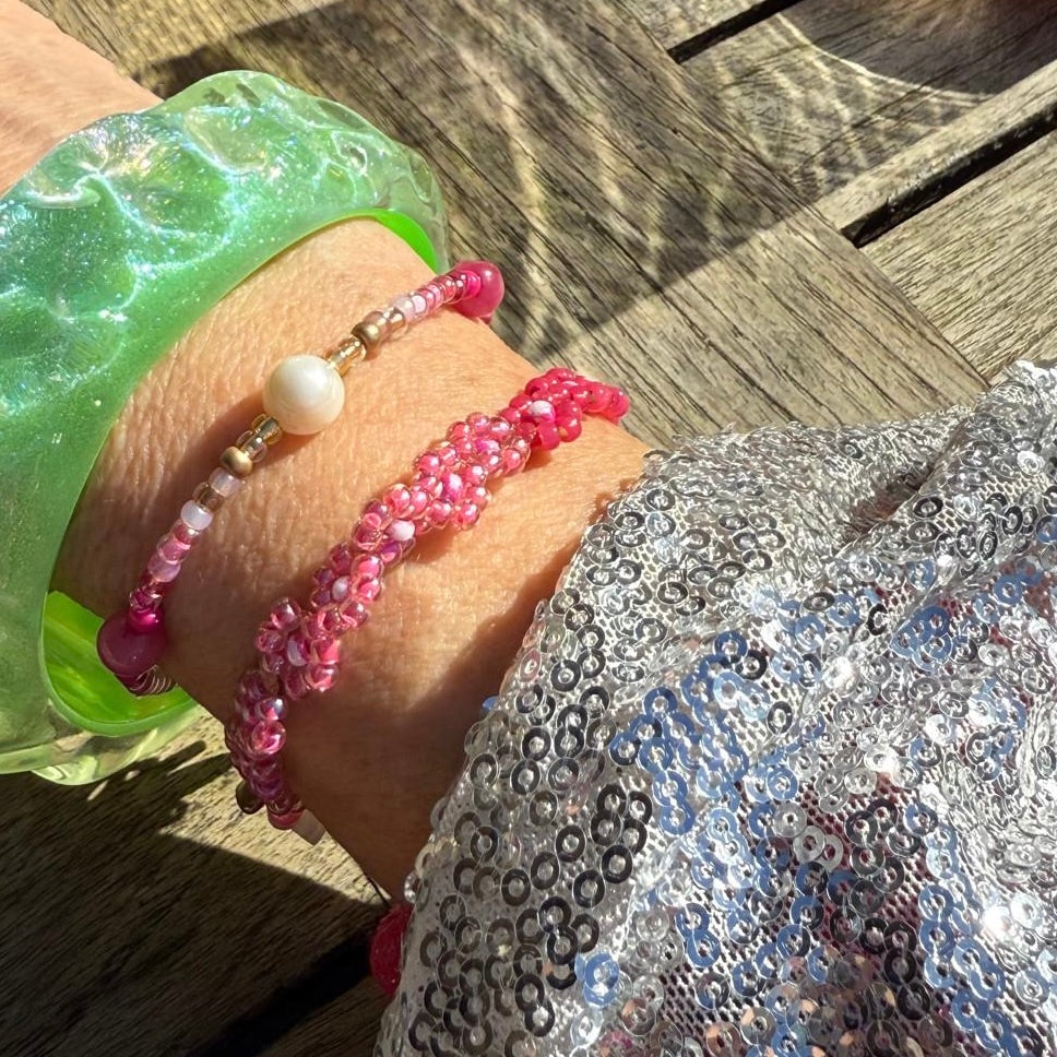 Close-up of a wrist wearing pink beaded bracelets on a wooden surface