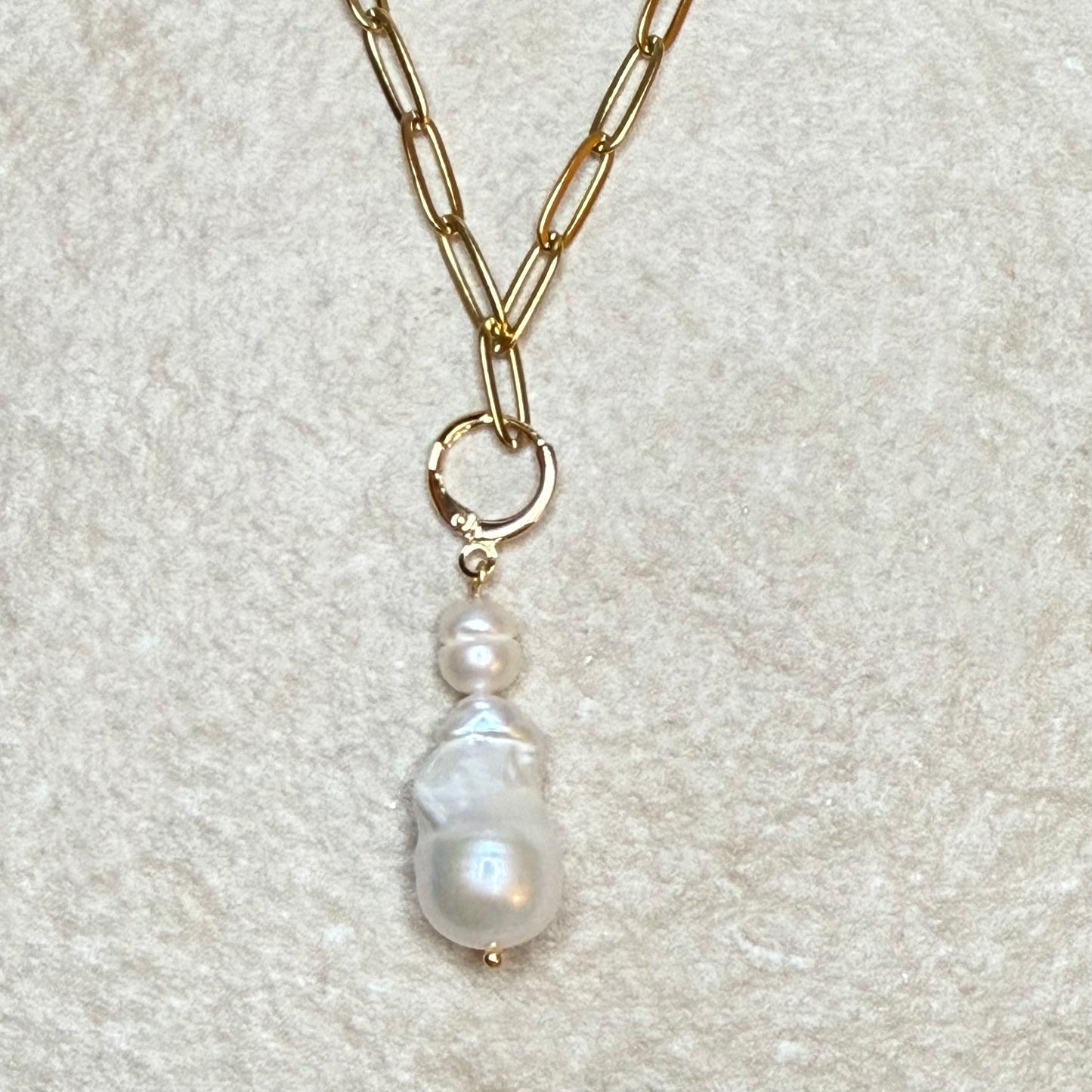 Gold chain necklace with a pearl pendant on a light gray background