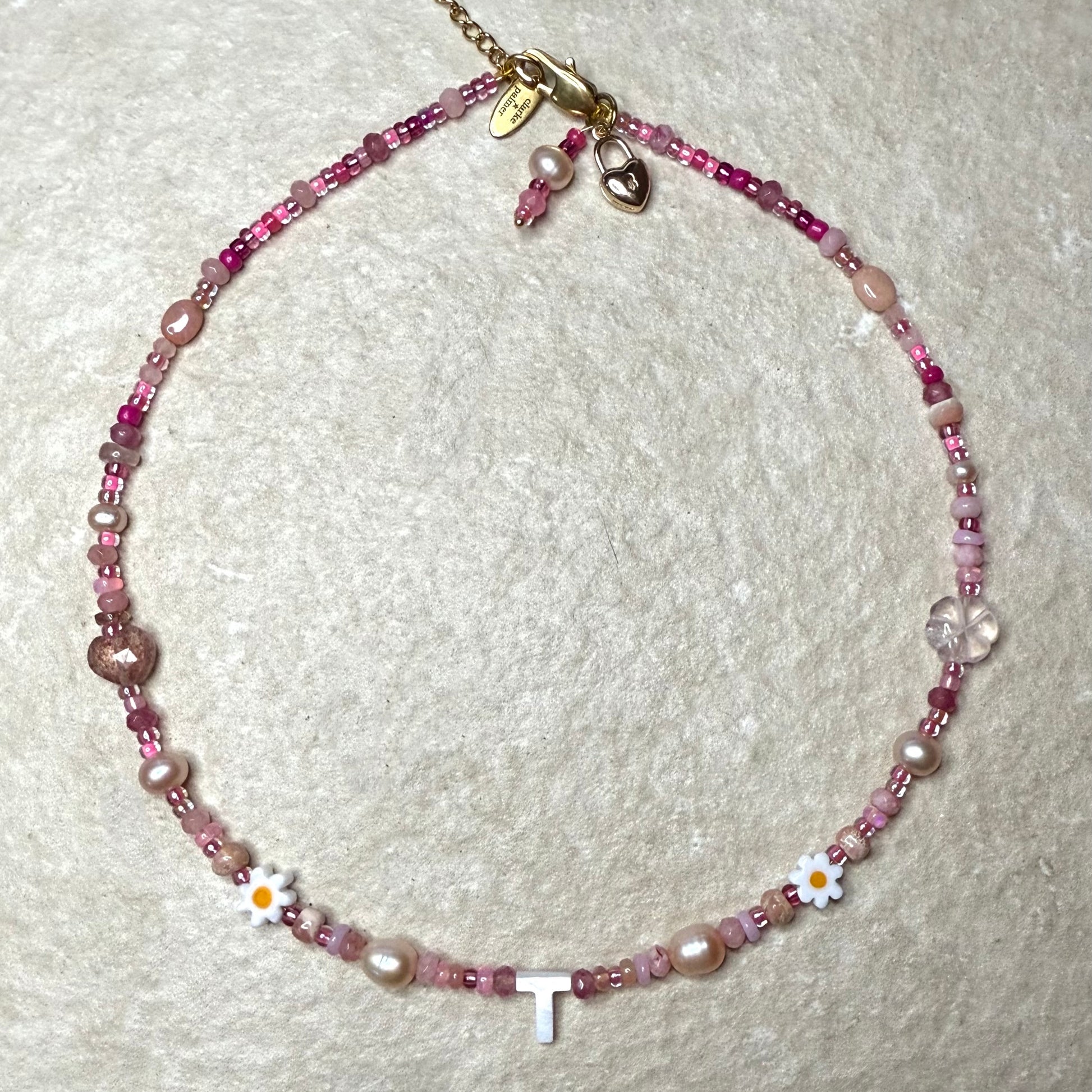 Detail of Necklace with pink gemstone beads and a letter 'T' on a textured white background